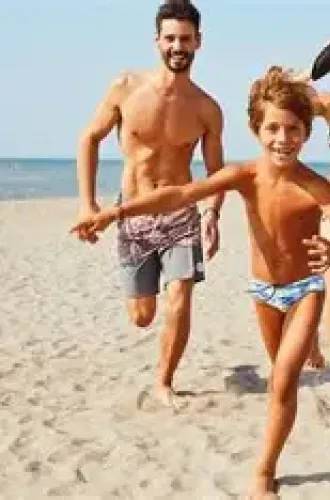 Famiglia felice corre sulla spiaggia, bambini giocano con palla colorata.