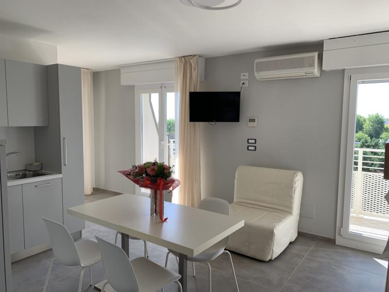 Appartamento moderno con cucina, tavolo, sedie, poltrona e balcone con vista.
