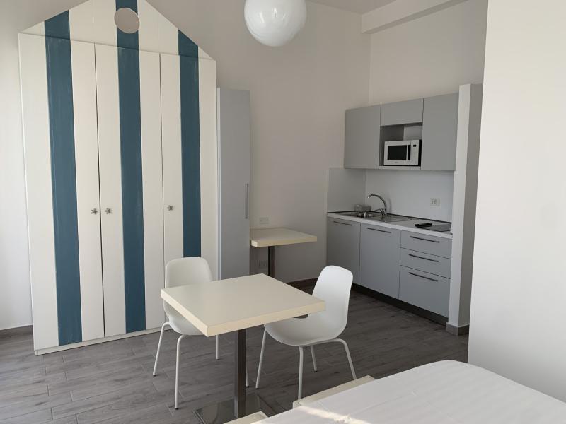 Monolocale moderno con cucina, tavolo e armadio a righe blu e bianche.