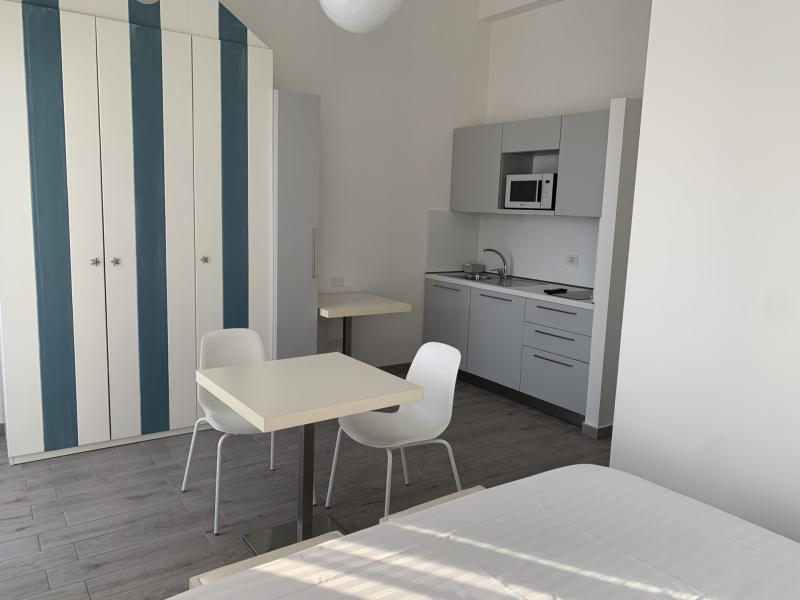 Monolocale moderno con cucina attrezzata, tavolo da pranzo e armadio a righe.